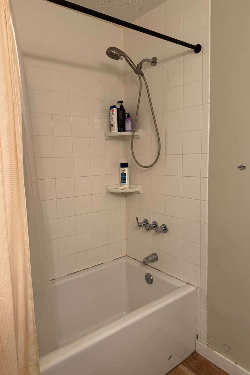 Clean bathroom with a showerhead, wall shelves, and a bathtub in neutral tones.