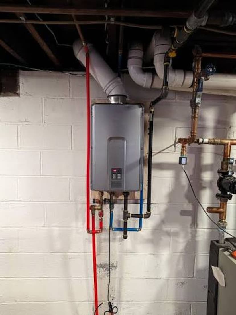 Tankless water heater installation in a basement with visible piping and connections.